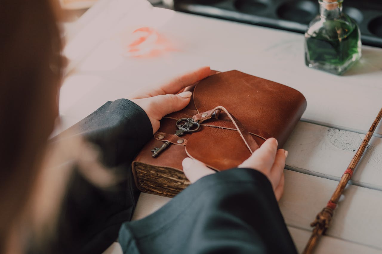 Hands hold a leather book with key on it, surrounded by magic wand and potion.